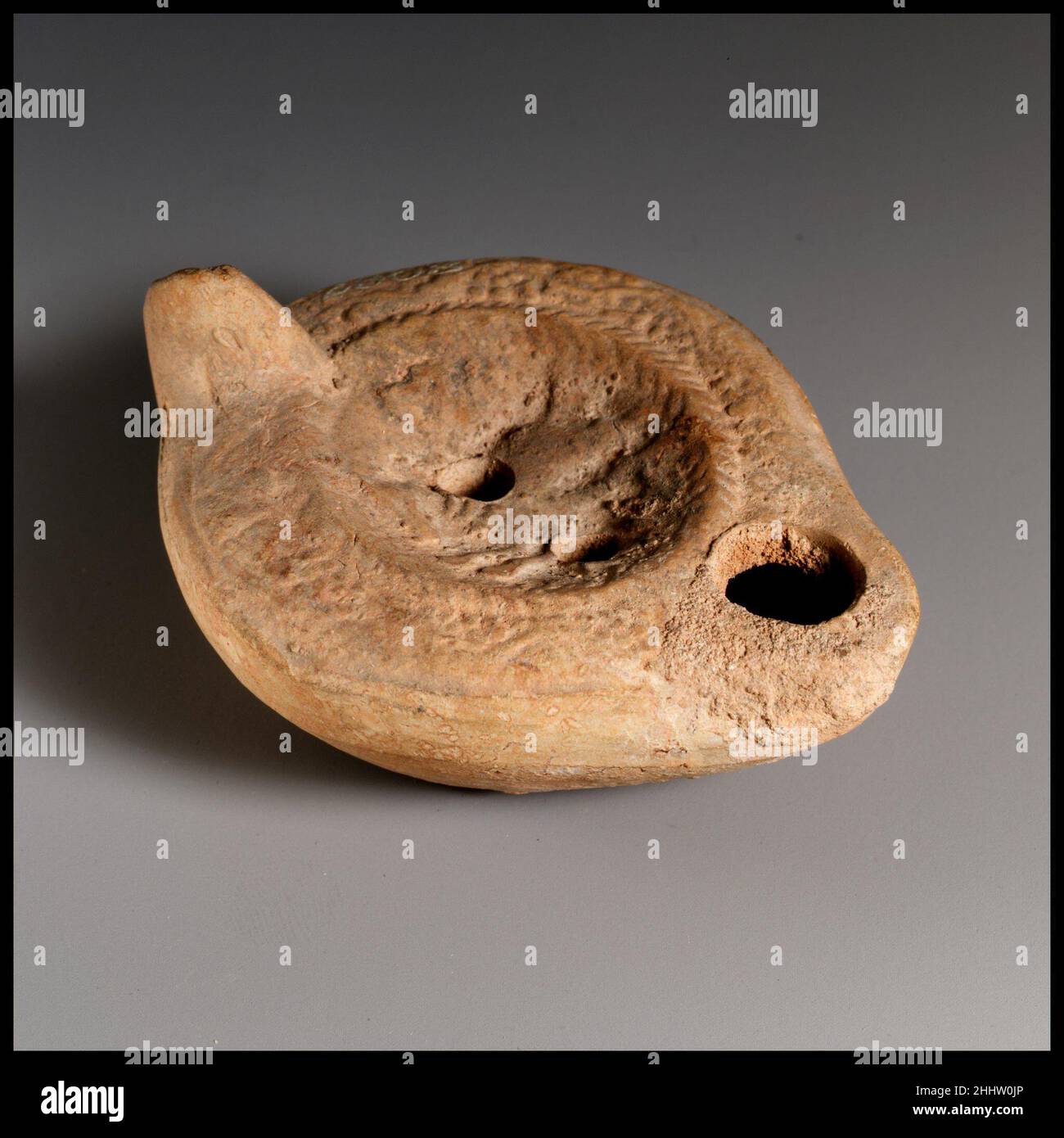 Lampada ad olio di terracotta 4th–5th secolo d.C. romana, cipriota Vessberg tipo 18. Impugnatura non forata. Realizzato in stampo. Disco: toro running rivolto a sinistra e con colletto ornato, fiancheggiato da entrambi i lati da corona di aringhe. Sopra il toro: Lettere indistinte (?); sotto il toro: Lettere greche in rilievo: A?Y. Due fori di riempimento. A spalla, tendine stilizzate di vite con grappoli di uva. Su base leggermente concava, lettere greche indistinte in rilievo: EYTYXHTOC (?). Buccia argilla.. Lampada ad olio di terracotta. Romano, cipriota. 4th–5th secolo d.C.. Terracotta. Tardo imperiale. Terracotte Foto Stock