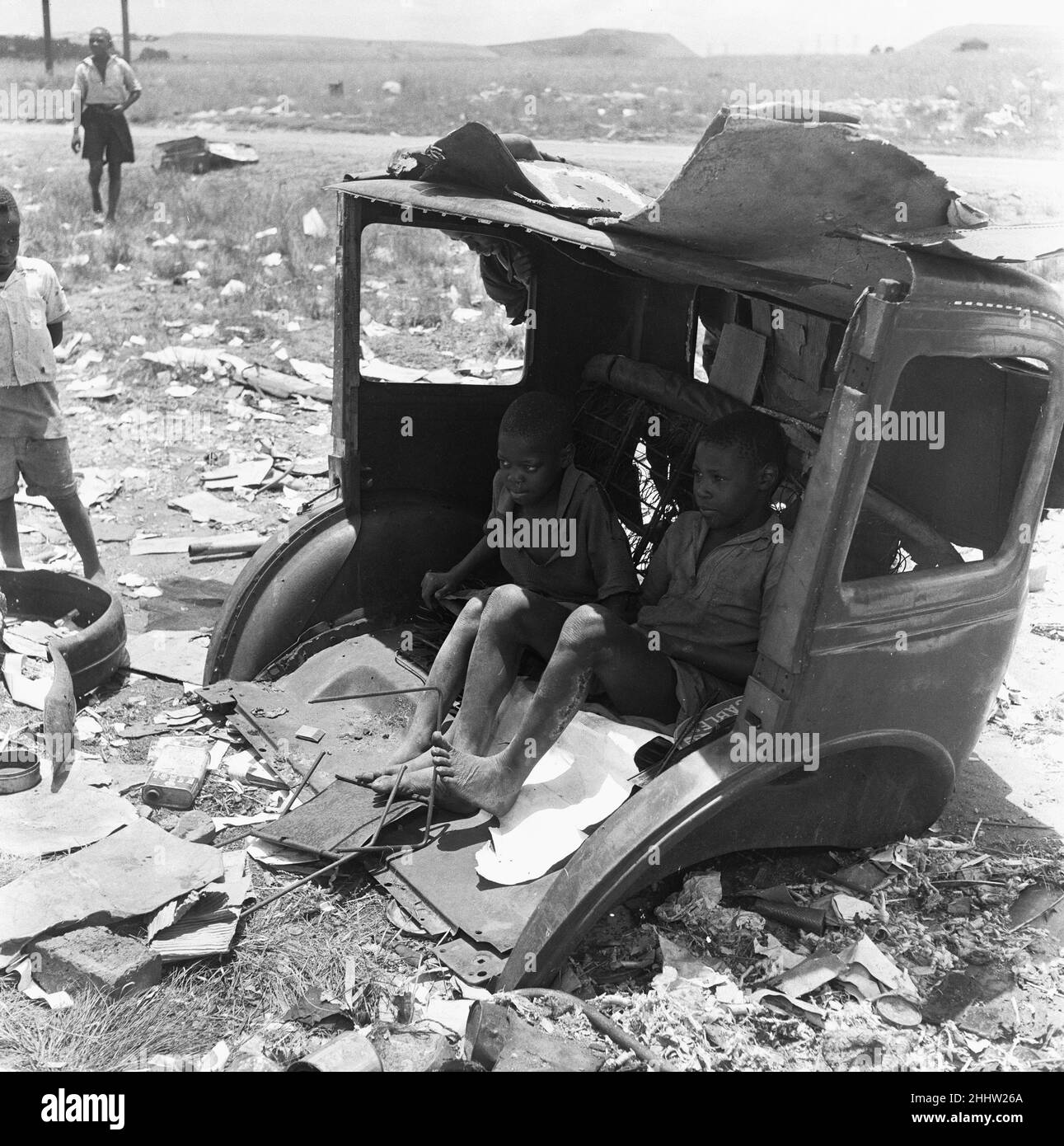 I bambini delle cittadine di Langa e Windermere sono stati visti qui per scovare la punta dei rifiuti di Orlando vicino a Città del Capo. Due ragazzi cercano ombra dal sole di mezzogiorno in un relitto di un'auto 4th febbraio 1955 Foto Stock