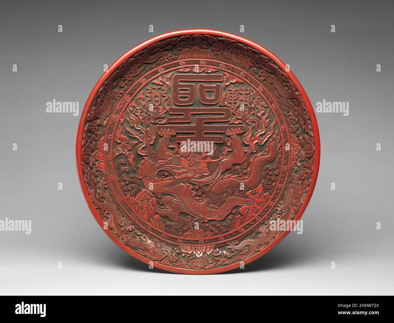 Vassoio con drago e personaggi cinesi 1522–1566 Cina questo vassoio è uno dei migliori prodotti delle officine ufficiali dell'era Jiajing. Probabilmente fu fatto nella prima parte del regno prima che l'immaginario Daoista cominciasse a dominare a corte. Il drago al centro sorregge il personaggio cinese sheng, che significa “divina” o “maestà imperiale”. I caratteri sopra di esso (fu a destra e bi a sinistra) generalmente indicano "da aggiungere" o "da supportare". Mentre possono essere usati per riferirsi ai capi ministri dell’imperatore, in questo caso possono riferirsi al drago, un noto simbolo dell’aut imperiale Foto Stock