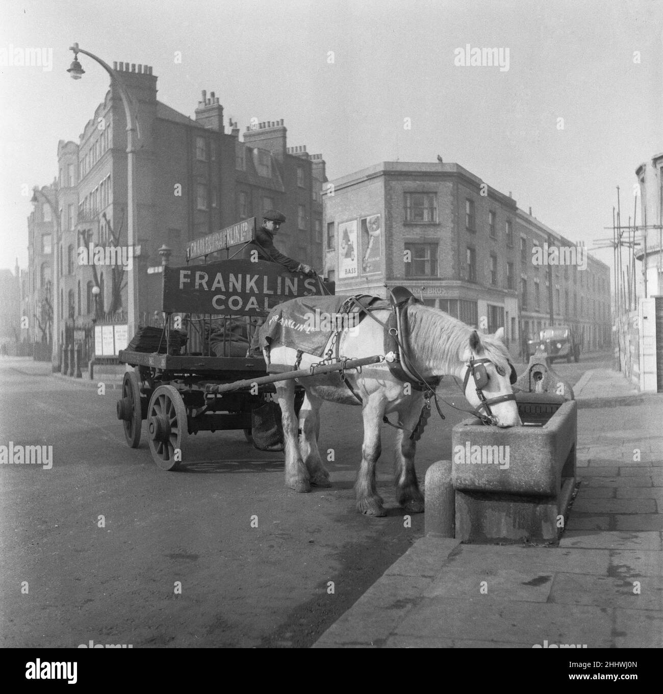 Bromley da Bow carbone mercante Charles Franklin cavalli e carro consegna prende una pausa e una bevanda di acqua dal trogolo durante il suo turno di consegna in Bow. 3rd marzo 1955 Foto Stock