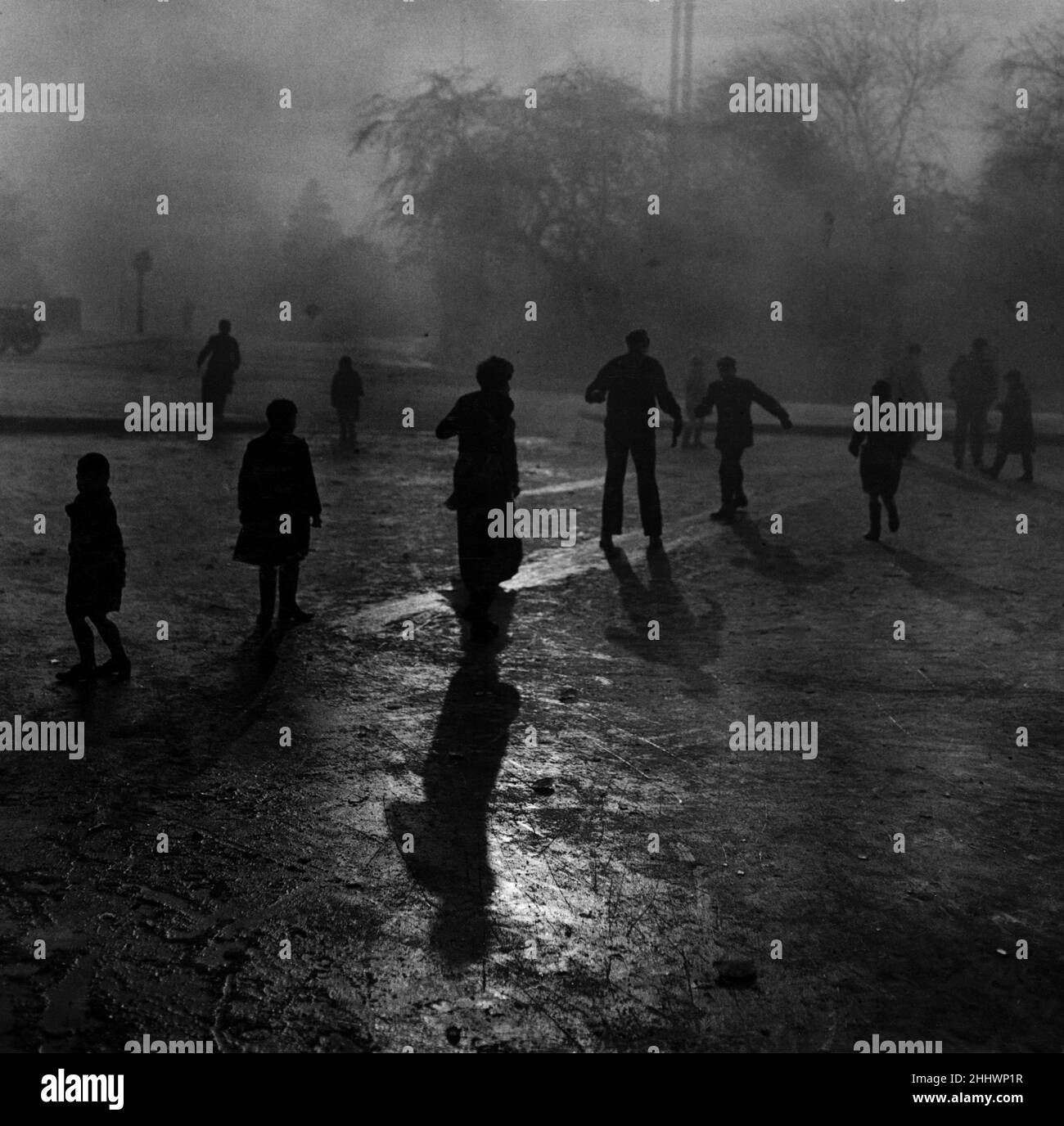 Nebbia e ghiaccio su Hampstead Heath. Ragazzi che scivolano sul ghiaccio nella nebbia agli stagni di Hampstead Heath. Anche se il tempo era wintry e la nebbia era spessa, la folla solita di piccoli ragazzi gravitò naturalmente agli stagni di Hampstead Heath quando uscì la parola che il ghiaccio era abbastanza denso da stare in piedi sopra. Là nonostante le condizioni del vino, 30 ragazzi piccoli dispari con la scorta usuale di cani piccoli hanno avuto un tempo meraviglioso scivolando sul ghiaccio. 7th dicembre 1952. Foto Stock