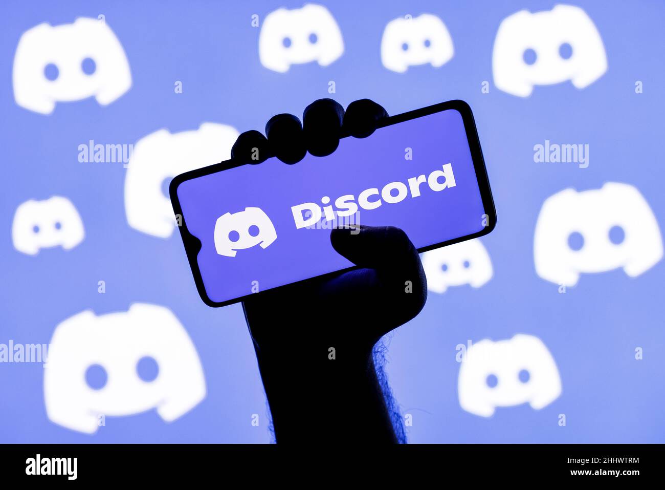 Smartphone con il logo della piattaforma di gioco sociale Discordia sullo schermo in una mano applaiata sullo sfondo dei logo Discordia Foto Stock