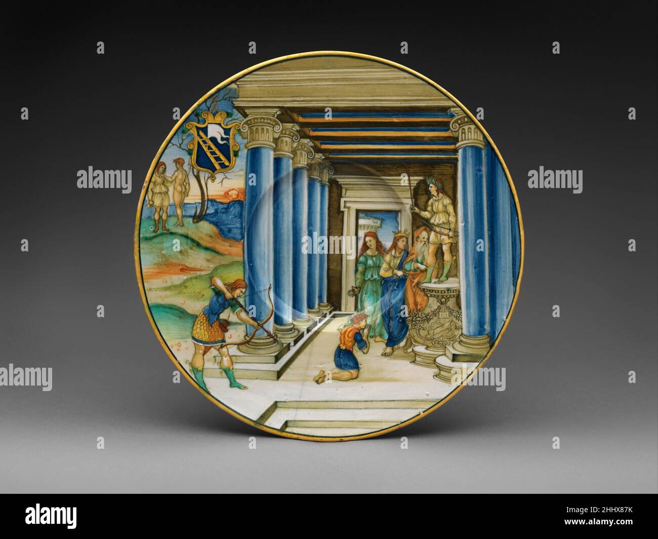 Piatto con Parigi uccidendo Achille e le braccia della famiglia Calini ca. 1525 Nicolo da Gabriele Sbraghe la mitologia classica e la storia biblica sono i temi più popolari della maiolica rinascimentale. Per l'ispirazione, i pittori hanno cercato stampe ampiamente diffuse, modificando con attenzione le composizioni rettangolari per meglio adattarsi alle superfici arrotondate e contornate della tavola. Qui, l'artista ha modificato una stampa spingendo gli elementi più importanti della storia, come il tallone vulnerabile di Achille, fino al bordo del piatto, in modo che restassero visibili indipendentemente dalla presenza di cibo. Piatto con Paris Ki Foto Stock