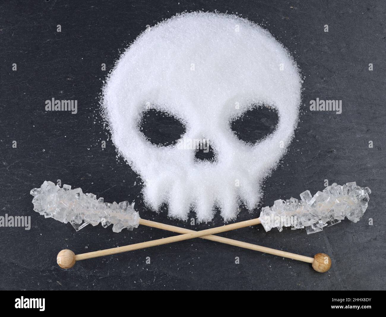 Cranio a forma di zucchero bianco raffinato e zucchero caramella incrociato su bastoni di legno su sfondo di ardesia nera, Foto Stock