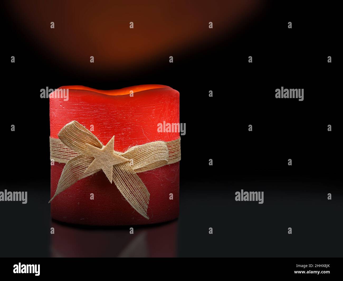 candela di natale rosso acceso con banda di iuta e stella su sfondo nero, illuminato decorazione di natale Foto Stock