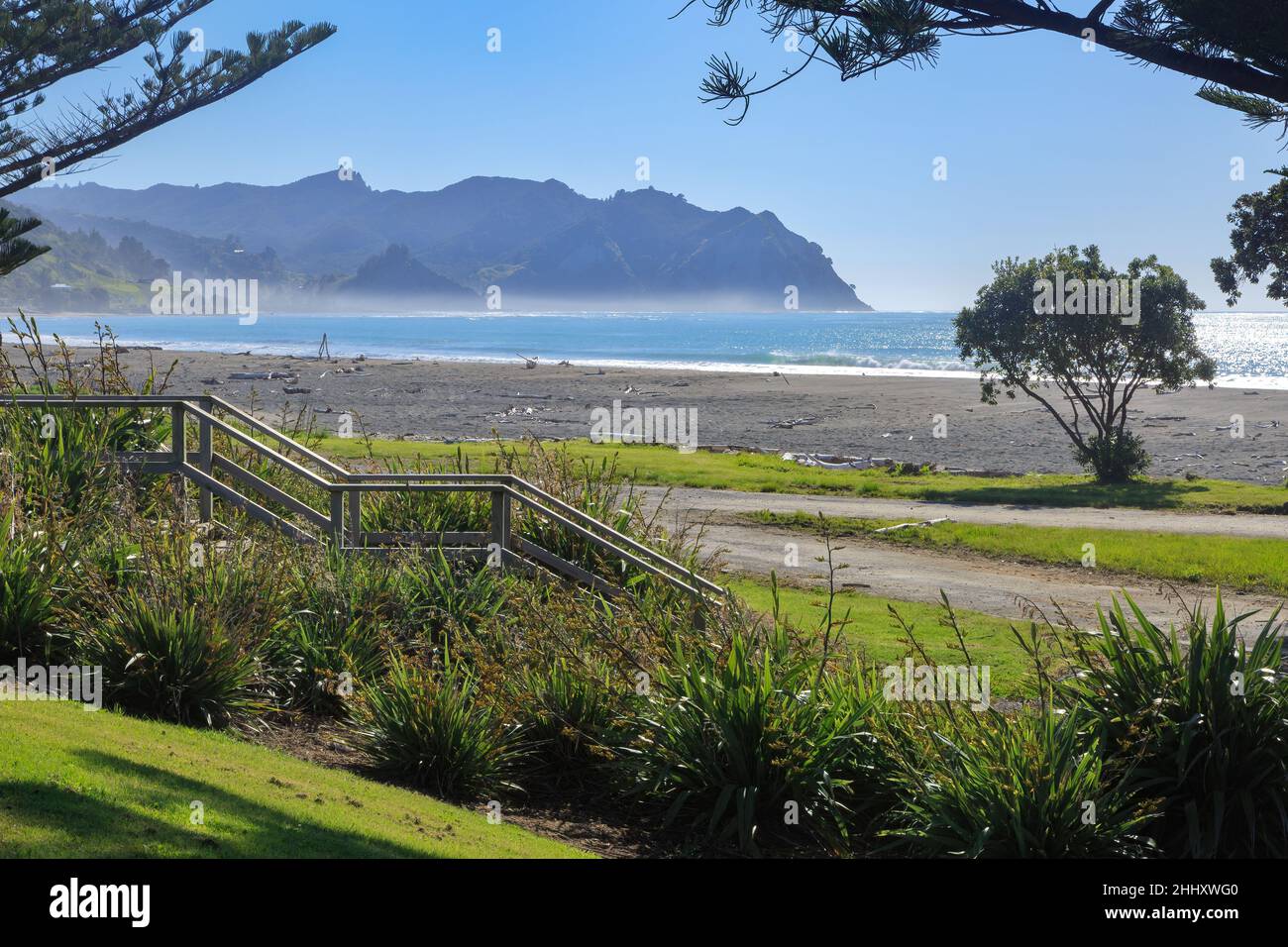 Una spiaggia soleggiata a Tokomaru Bay nella regione di Gisborne, Nuova Zelanda. I gradini di legno conducono alla sabbia Foto Stock