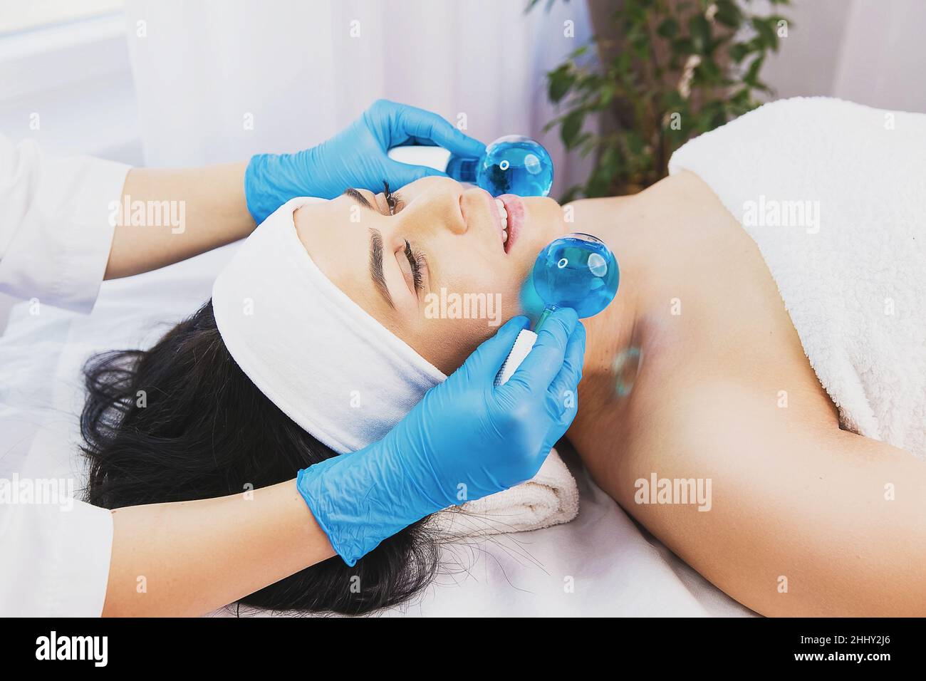 calmare la paziente donna che subisce le procedure di massaggio cosmetico viso per ringiovanire la pelle viso e medico utilizzando strumenti cosmetici, palline di ghiaccio criogenico Foto Stock