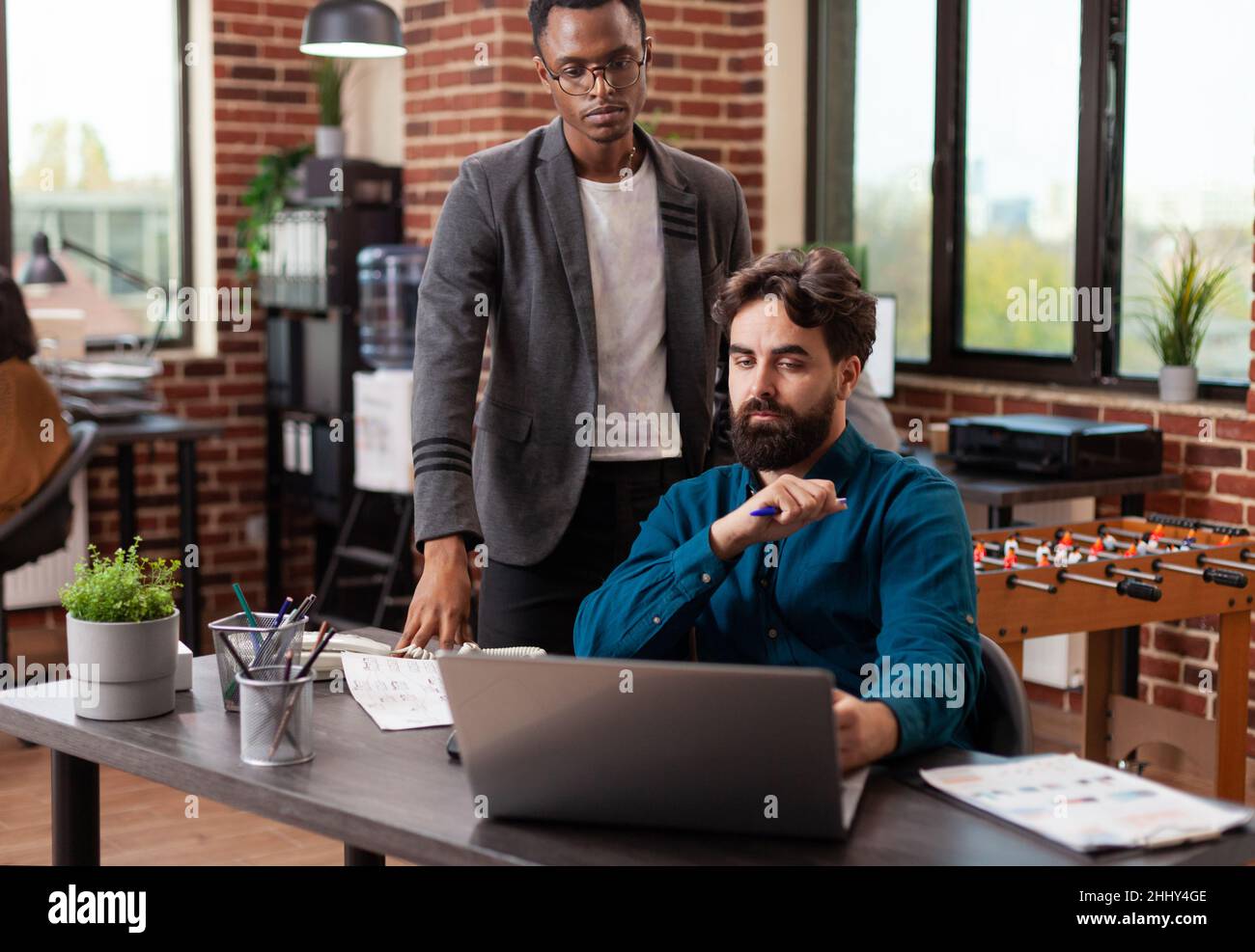 Uomini d'affari multirazziale brainstorming idee per il progetto di marketing mentre si lavora alla strategia aziendale in mattone muro startup ufficio. Team diversi che analizzano le statistiche e pianificano la collaborazione aziendale Foto Stock