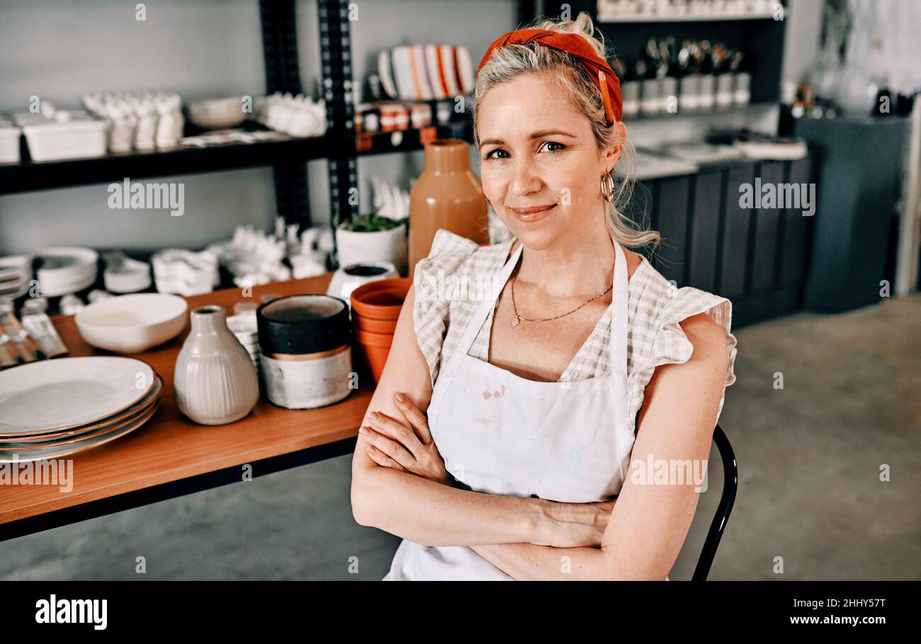Sto vivendo la mia vita migliore. Ritratto corto di una donna matura attraente seduta con le braccia ripiegate nella sua bottega di ceramica. Foto Stock