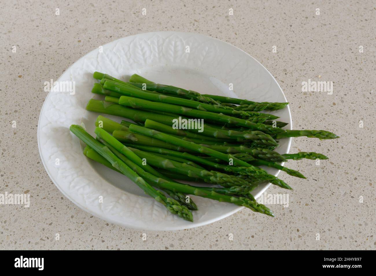 Asparagi - deliziose, fresche, teneri, lance di asparagi verdi - su un piatto bianco - sfondo beige Foto Stock