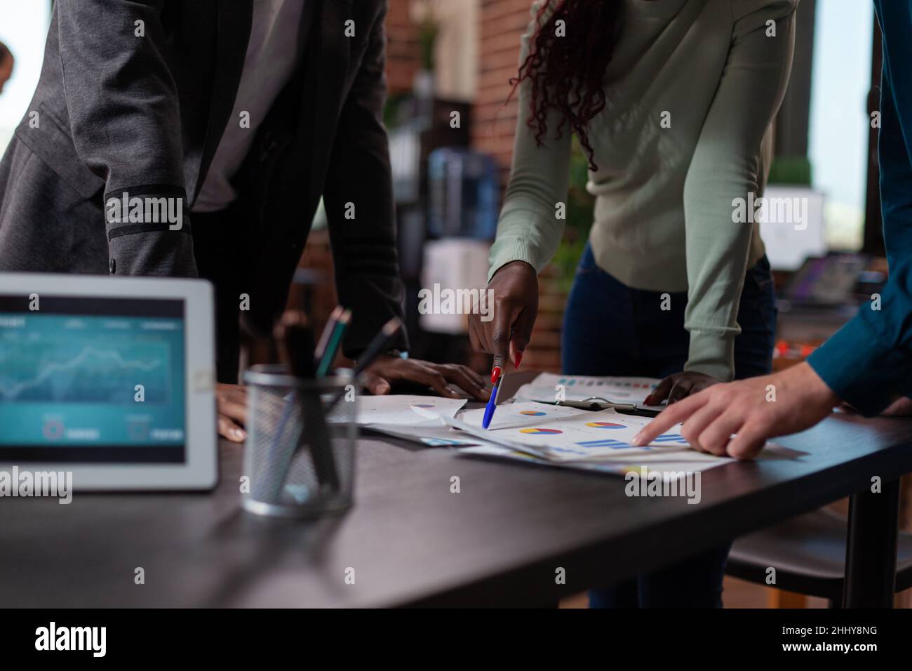 Primo piano di diversi team che analizzano le carte con statistiche di marketing che lavorano al progetto aziendale in un ufficio a muro di mattoni. Gli uomini d'affari multietnici brainstorming idee durante la collaborazione aziendale Foto Stock