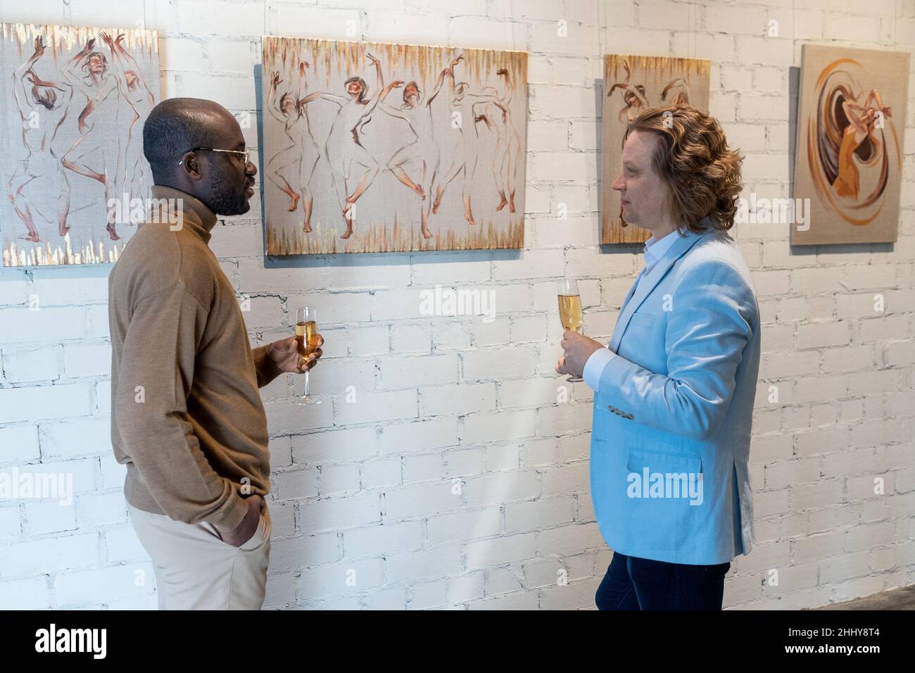 Due uomini in piedi vicino al muro con dipinti che bevono champagne e discutere di arte moderna Foto Stock