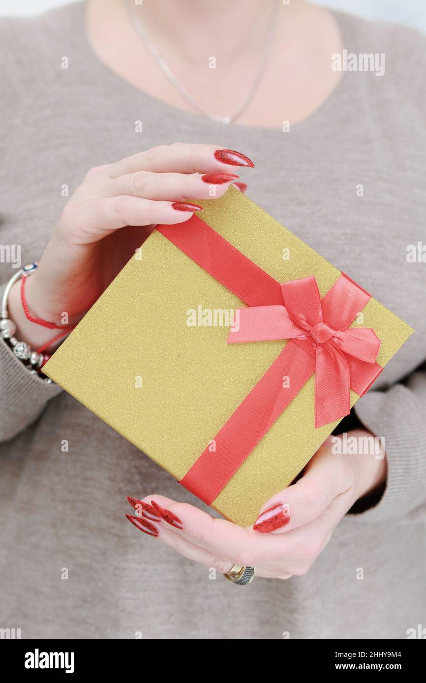 Le mani femminili con le unghie lunghe e il manicure rosso tengono una scatola con un regalo per la festa. Foto Stock