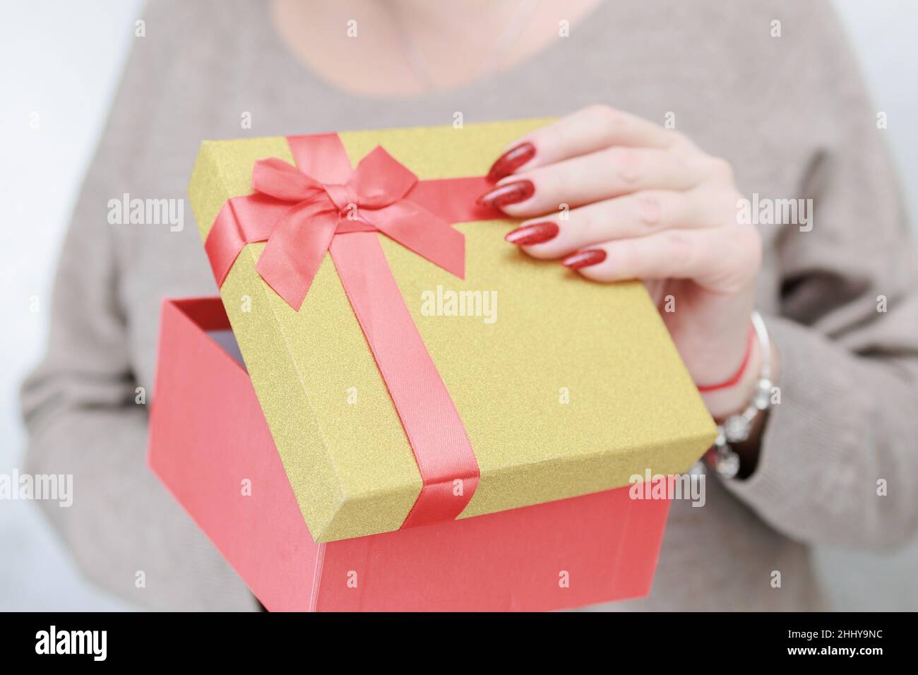 Le mani femminili con le unghie lunghe e il manicure rosso tengono una scatola con un regalo per la festa. Foto Stock