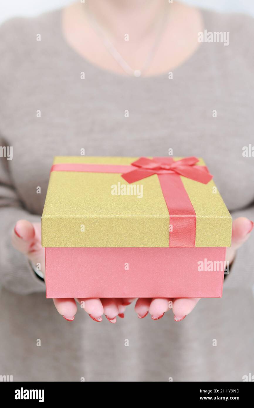 Le mani femminili con le unghie lunghe e il manicure rosso tengono una scatola con un regalo per la festa. Foto Stock