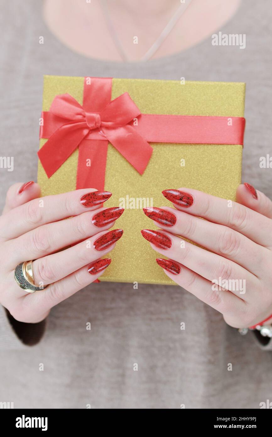 Le mani femminili con le unghie lunghe e il manicure rosso tengono una scatola con un regalo per la festa. Foto Stock