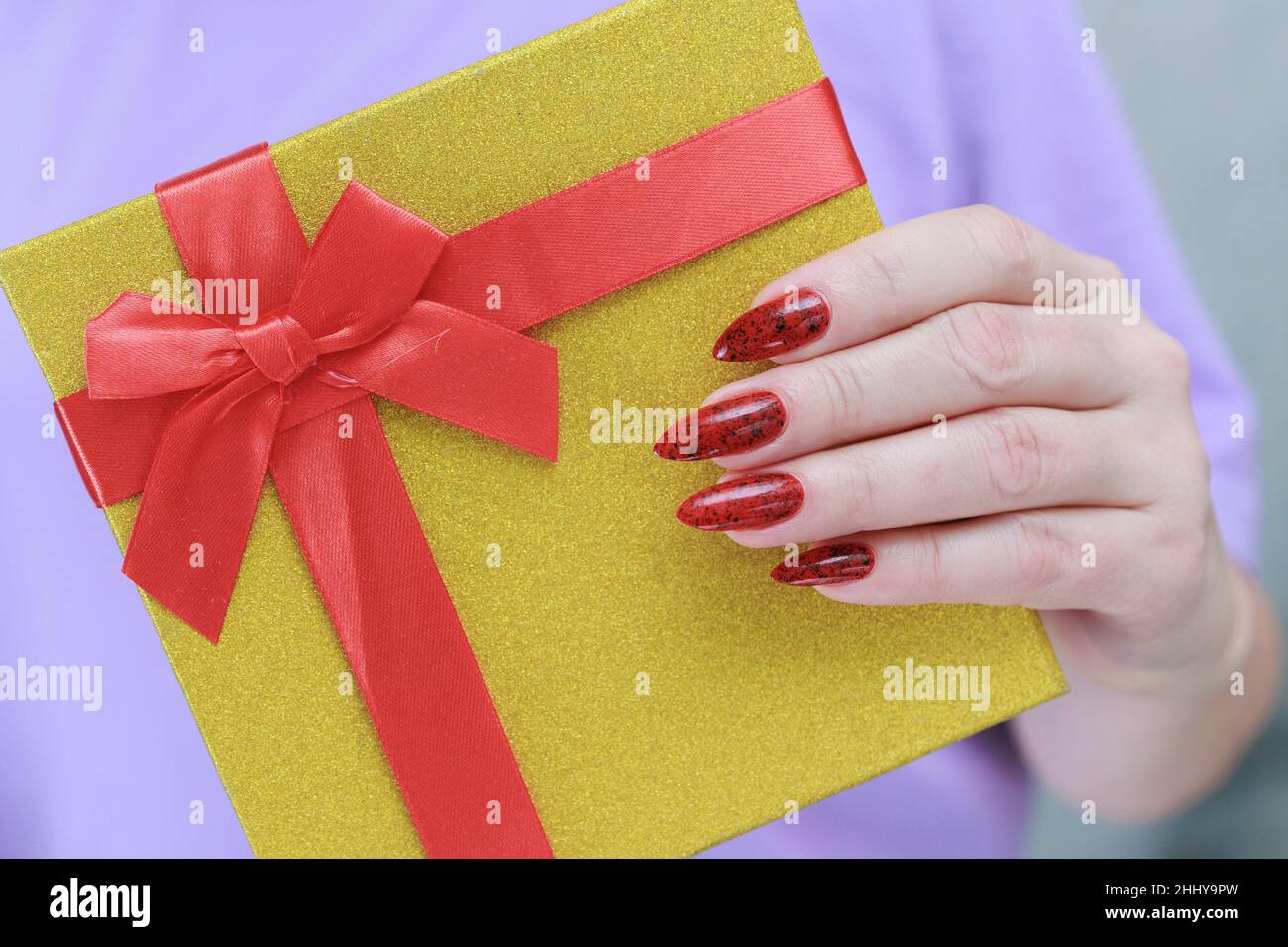 Le mani femminili con le unghie lunghe e il manicure rosso tengono una scatola con un regalo per la festa. Foto Stock