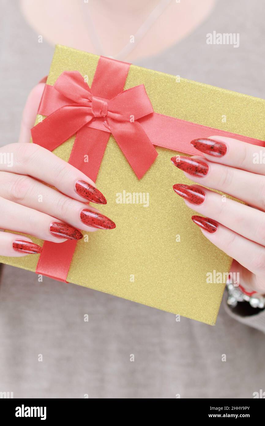 Le mani femminili con le unghie lunghe e il manicure rosso tengono una scatola con un regalo per la festa. Foto Stock