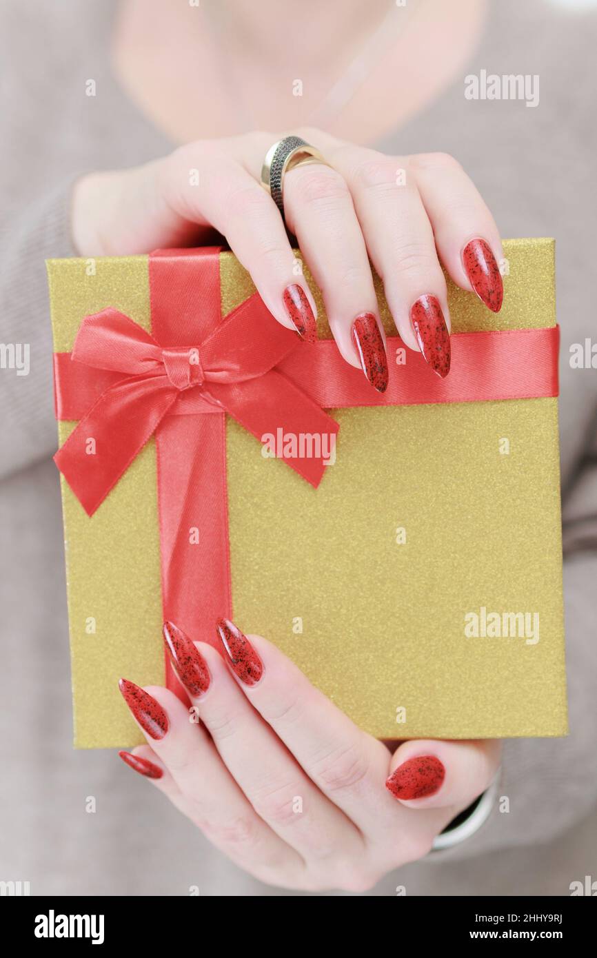 Le mani femminili con le unghie lunghe e il manicure rosso tengono una scatola con un regalo per la festa. Foto Stock