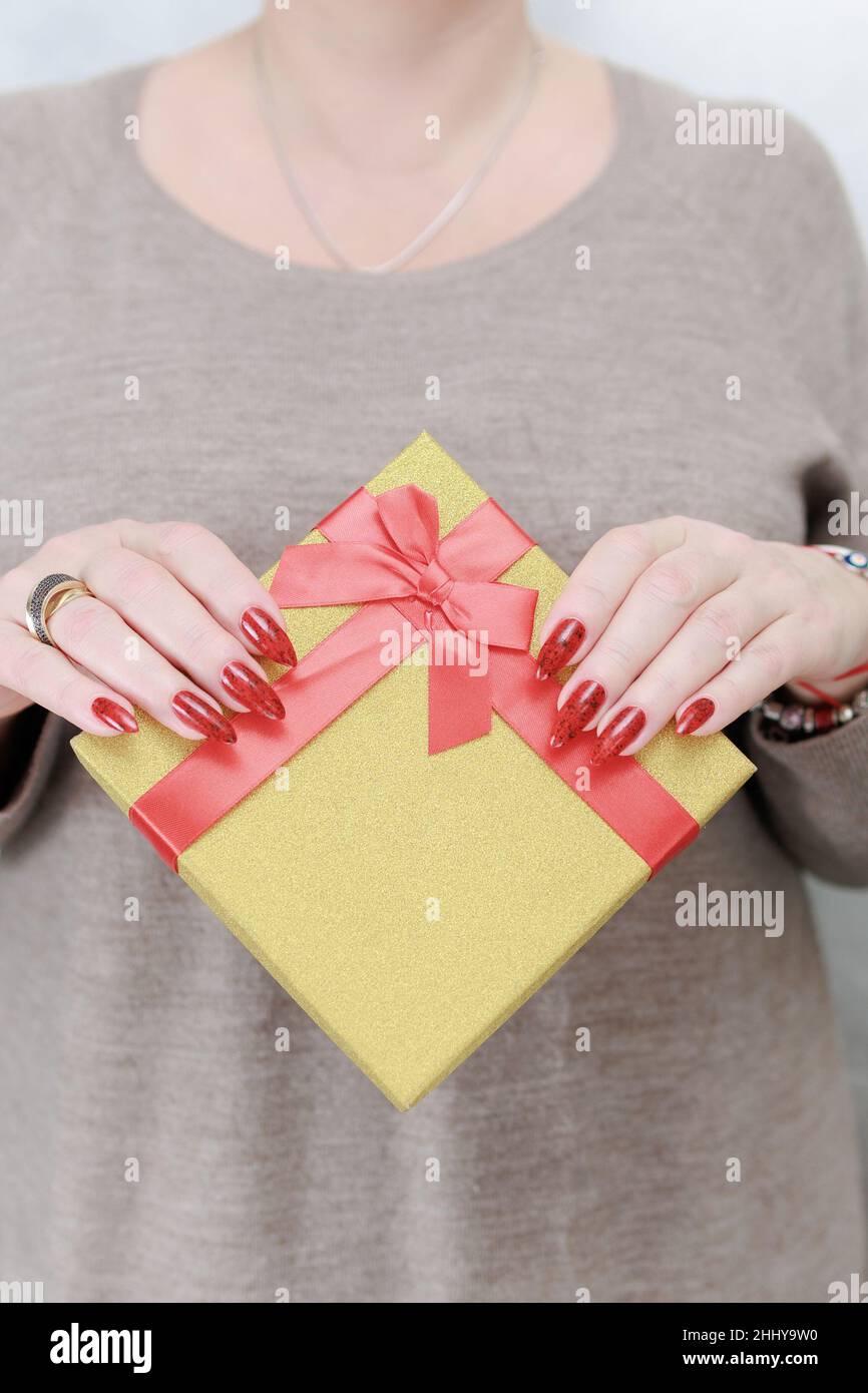 Le mani femminili con le unghie lunghe e il manicure rosso tengono una scatola con un regalo per la festa. Foto Stock