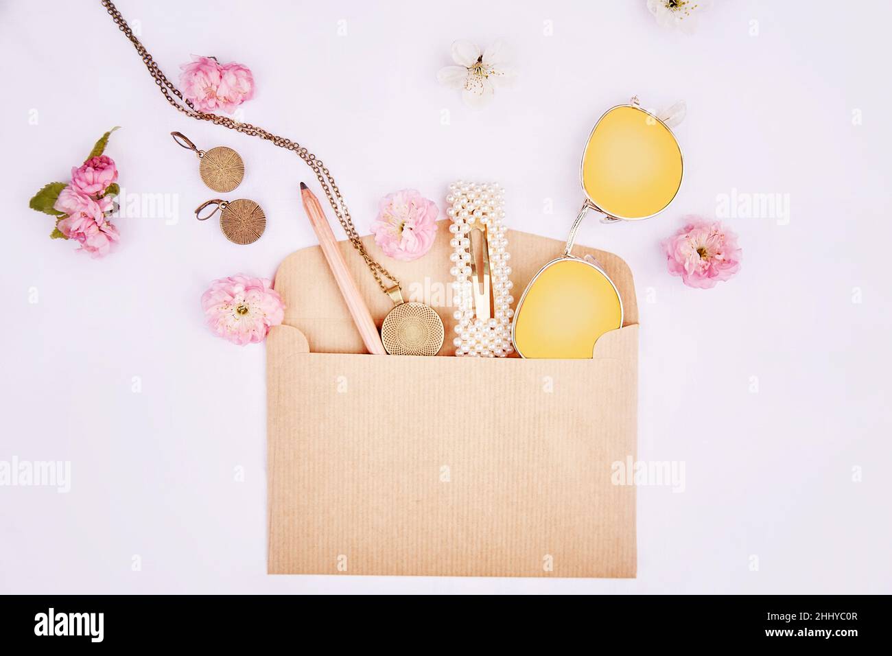 Splash di accessori donna da busta con fiori rosa. Occhiali da sole, accessori, forcina, orecchini, lampada da collo, matita per trucco su tessuto sfondo bianco. 8 del concetto di marzo. Foto Stock