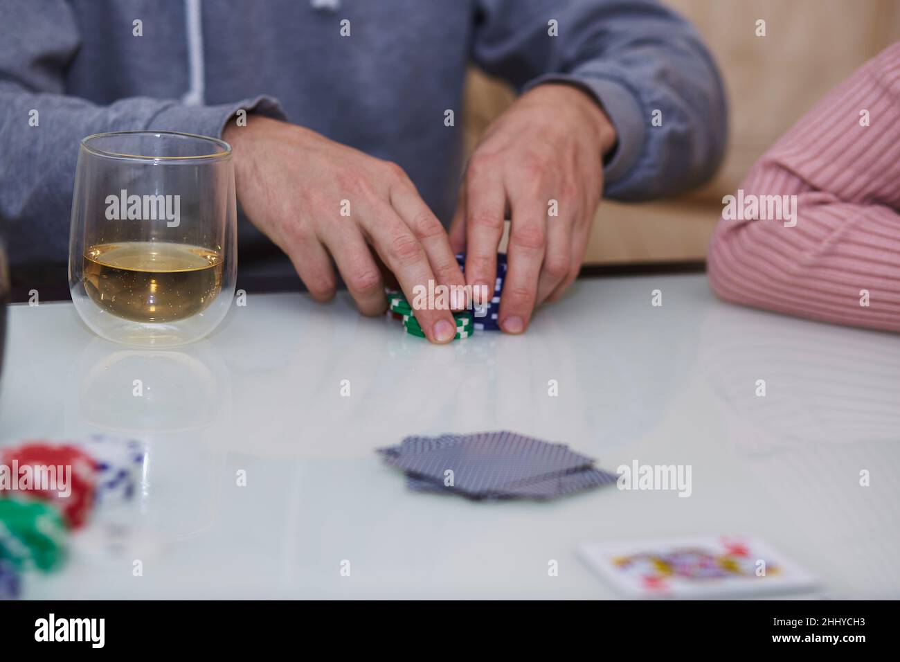 L'uomo ha le mani in un gioco di poker. Chip, carte, bicchiere di whiskey sul tavolo con riflessione. Fotografia di stile di vita. Poker club. Foto Stock