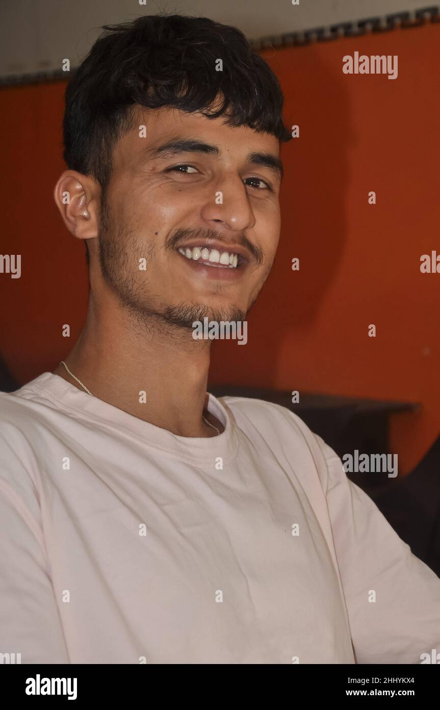 Primo piano di un giovane indiano dall'aspetto bello sorridendo, seduto in interni con la macchina fotografica Foto Stock