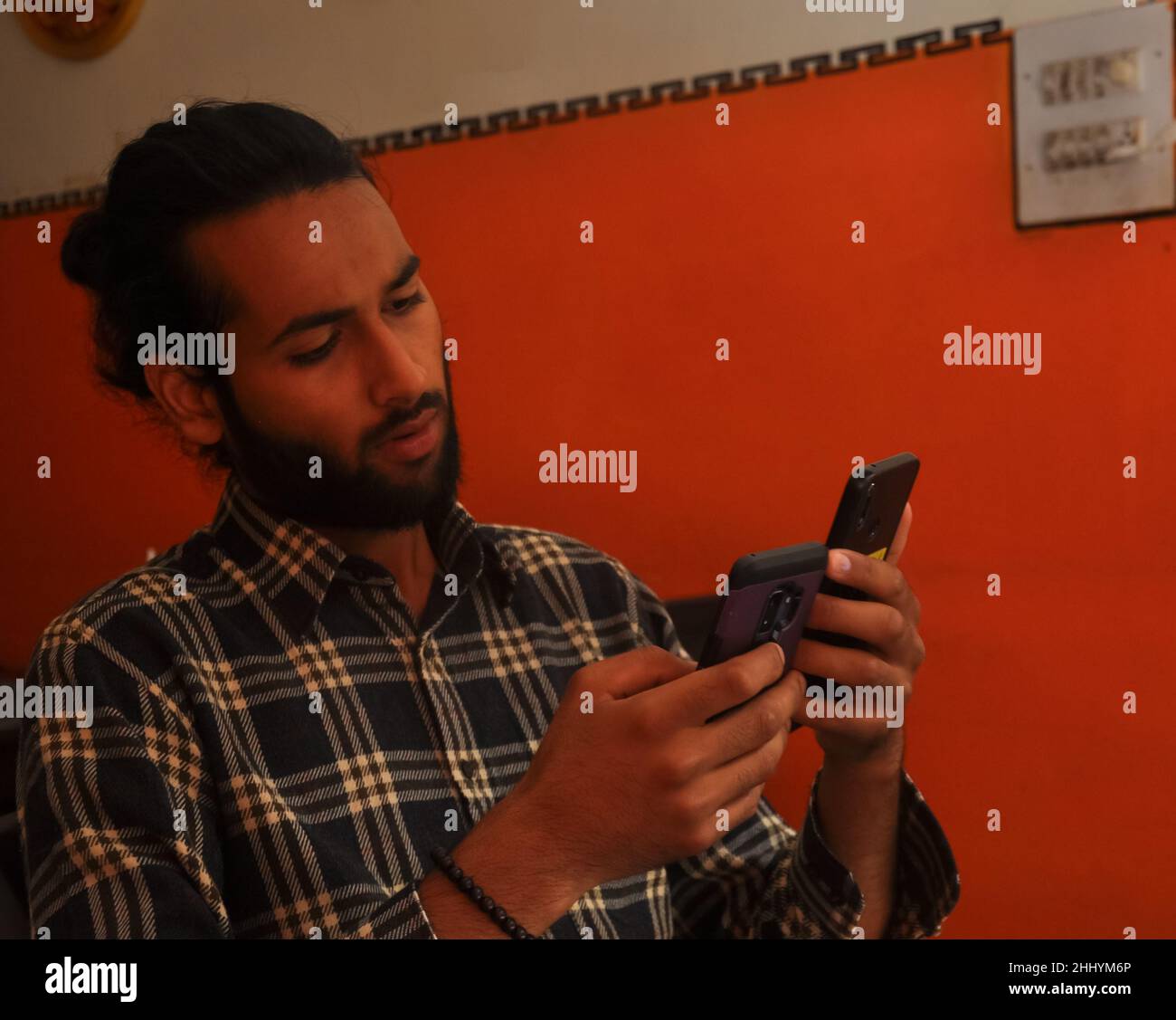 Primo piano vista laterale di un bel bearded uomo con capelli bun, tenendo due telefoni - Stock Photo Foto Stock