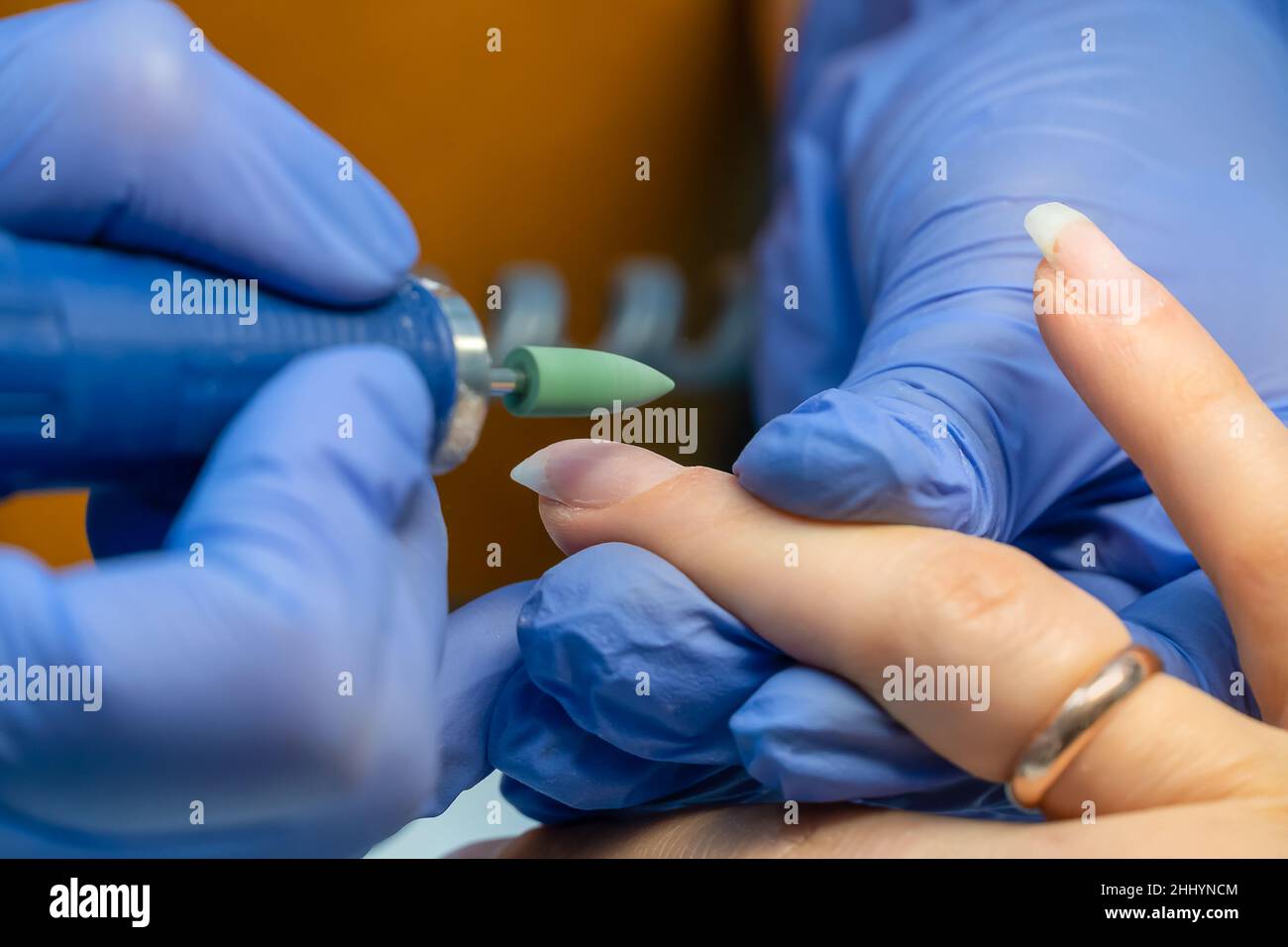 Manicure master in guanti blu macina le unghie con un dispositivo speciale prima di rivestire gel lucidante, macro. Foto Stock