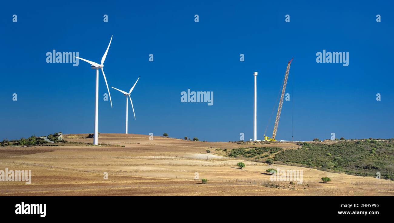 Costruzione di turbine eoliche presso la fattoria eolica di Oreites a Cipro. Paesaggio di campagna contro il cielo blu Foto Stock