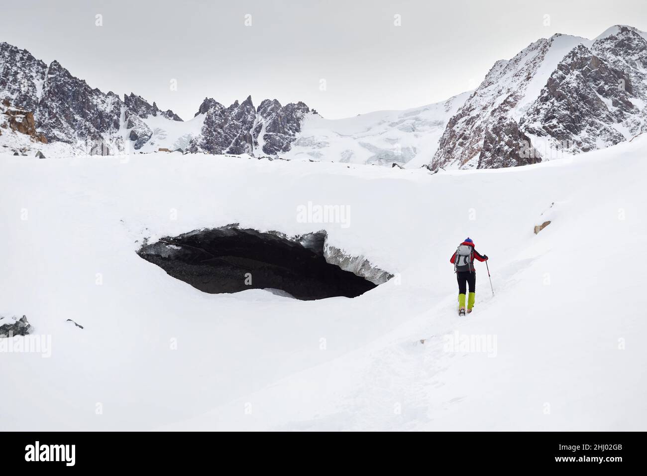 Turista con zaino vicino ghiaccio grotta arco al ghiacciaio in bellissimo paesaggio di valle di montagna coperta di neve in Almaty, Kazakhstan Foto Stock