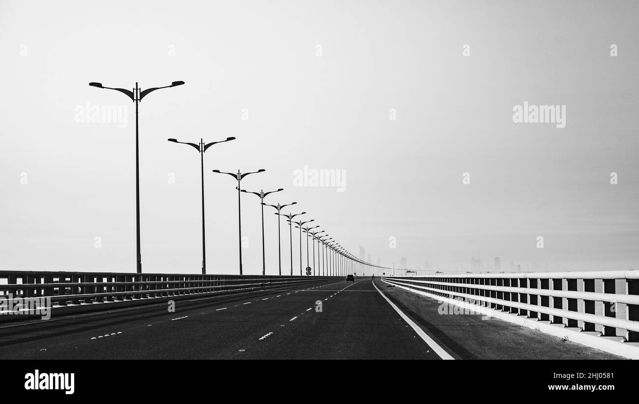 Un'immagine in scala di grigi di una fila di poli di luce su un ponte Foto Stock