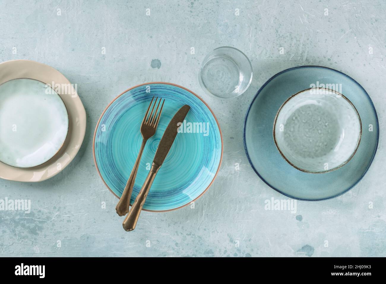 Stoviglie moderne con posate. Un piatto blu vibrante con una forcella e un coltello, un colpo superiore con un bicchiere e altro vasellame Foto Stock