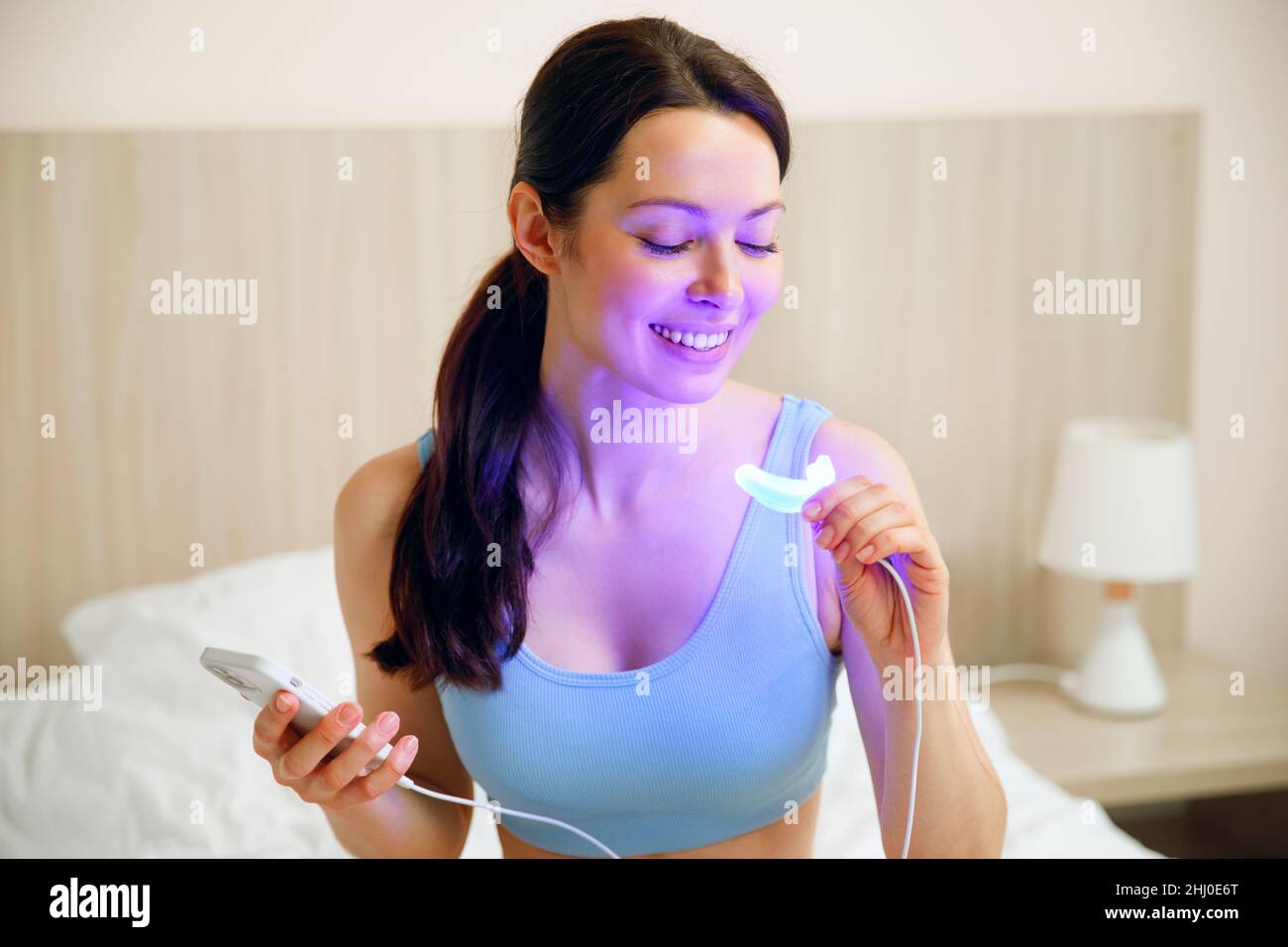 Una giovane donna usa un complesso sbiancante per la casa denti sbiancanti. Lampada UV USB per sbiancamento dei denti. Foto Stock