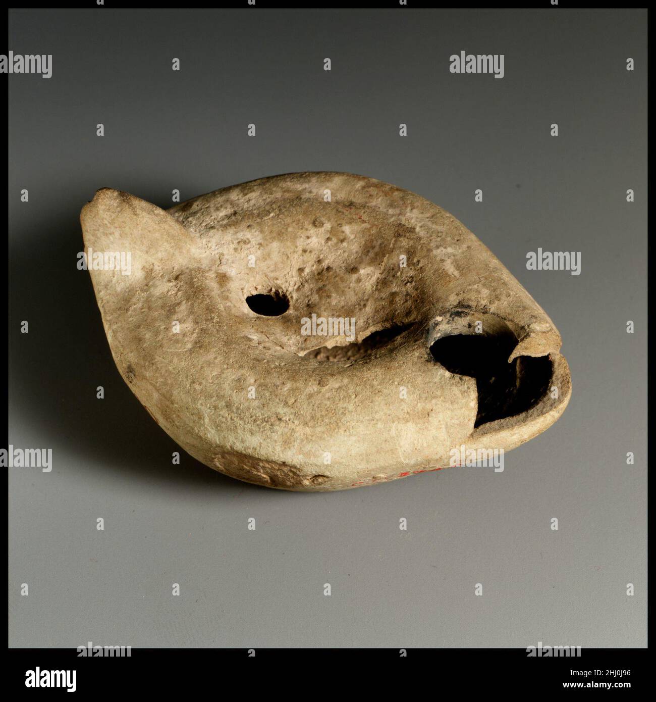 Lampada ad olio di terracotta 4th–5th secolo d.C. Vessberg romano tipo 18. Impugnatura non forata. Realizzato in stampo. Discus: Incerto; intorno al bordo, la corona di herringbone (?). Foro di archiviazione singolo in alto al centro. Spalla: Incerta. Base indefinita, leggermente concava, con cerchio di lettere greche in rilievo. Foro nel disco, parte anteriore superiore dell'ugello mancante e danni alla superficie sul lato sinistro del corpo. Argilla rosa con buccia giallastra. Lampada ad olio di terracotta. Romana. 4th–5th secolo d.C.. Terracotta. Tardo imperiale. Terracotte Foto Stock