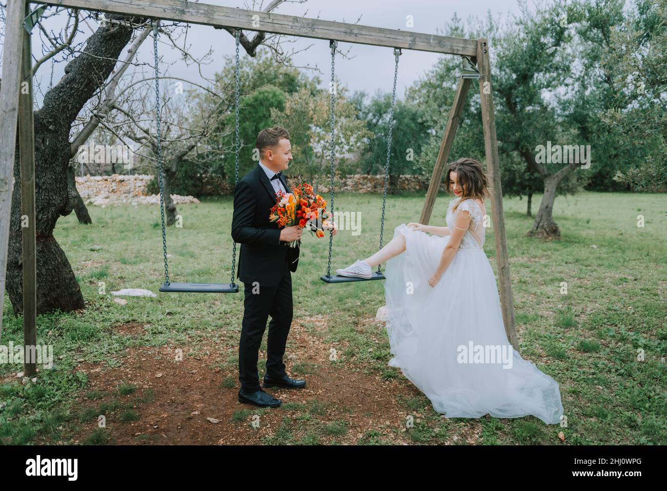 Felice coppia sorridente di stile che cammina in Toscana, Italia il giorno del matrimonio. SPOSI NOVELLI CON L'ALTALENA NEL PARCO. La sposa e lo sposo camminano giù il Foto Stock