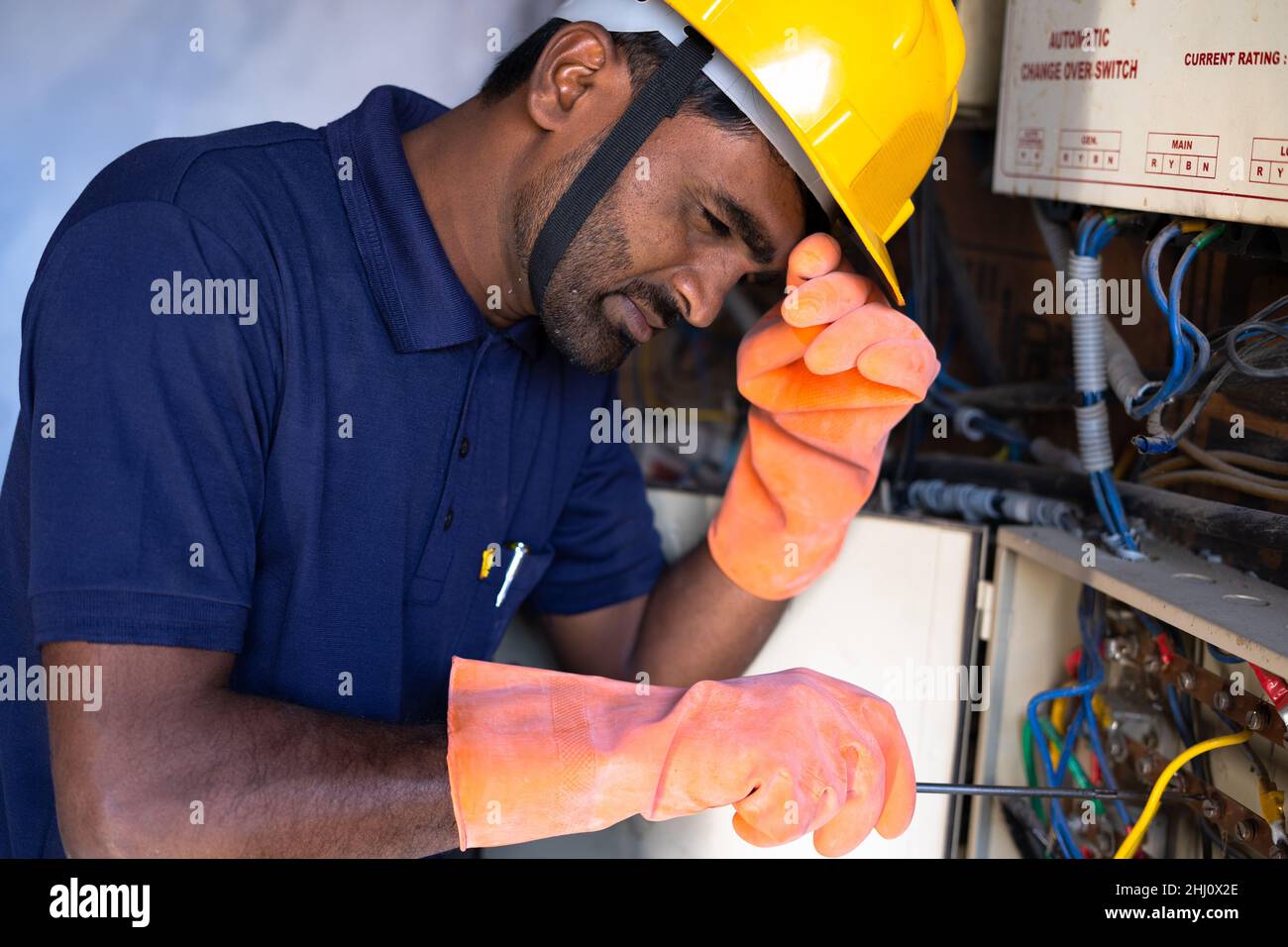 Elettricista o riparatore indiano stanco di lavorare mentre ripara o ripara i collegamenti sul posto di lavoro - concetto di lavoro duro, overworking e manutenzione Foto Stock