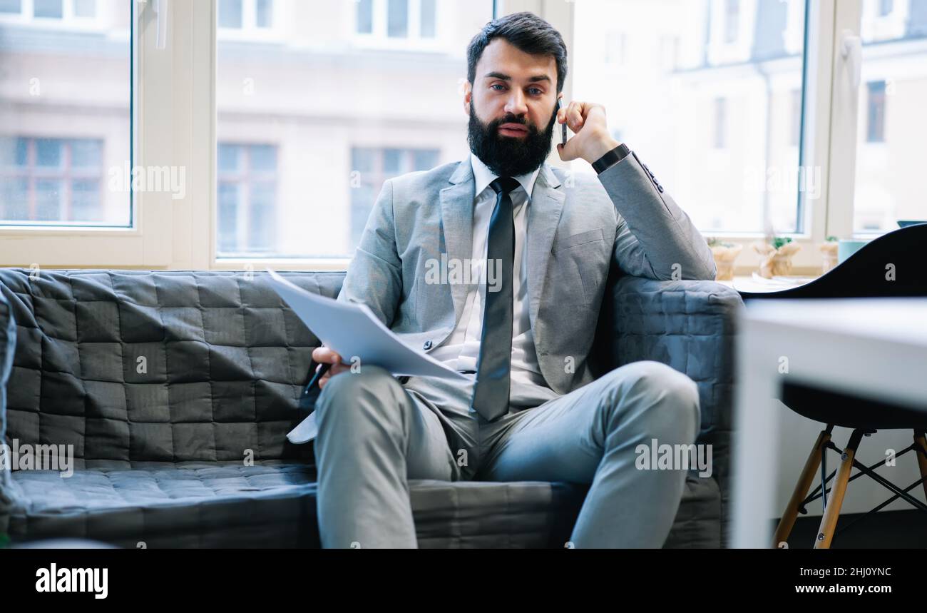Uomo d'affari stanco con documenti che parlano al telefono Foto Stock