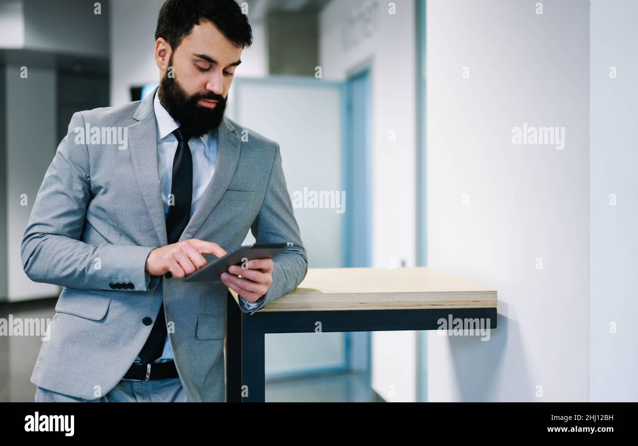 Sicuro uomo d'affari adulto che naviga il tablet mentre si appoggia sul tavolo Foto Stock