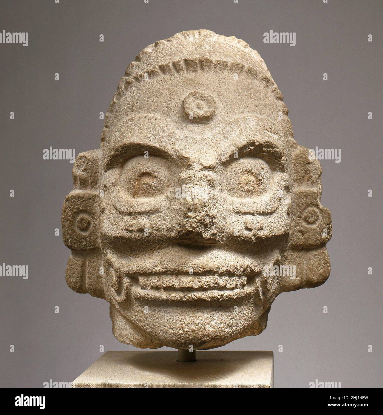 Head of a Rain God 11th–10th Century Maya questa testa monumentale scolpita da calcare raffigura un essere soprannaturale. Il soggetto è definito da caratteristiche scheletriche e indossa grandi auricolari e un archetto a perline. I capelli lunghi sono trattenuti e indicati da profonde incisioni che scorrono verso il retro della testa. Un boss circolare domina la fronte, rappresentando probabilmente un gioiello rotondo appeso in basso dalla fascia. Questa testa, ora staccata, probabilmente apparteneva ad una scultura architettonica in alto rilievo come parte di una facciata o come monumento indipendente. Divinità come quella qui raffigurata sono state viste Foto Stock Head of a Rain God 11th–10th Century Maya questa testa monumentale scolpita da calcare raffigura un essere soprannaturale. Il soggetto è definito da caratteristiche scheletriche e indossa grandi auricolari e un archetto a perline. I capelli lunghi sono trattenuti e indicati da profonde incisioni che scorrono verso il retro della testa. Un boss circolare domina la fronte, rappresentando probabilmente un gioiello rotondo appeso in basso dalla fascia. Questa testa, ora staccata, probabilmente apparteneva ad una scultura architettonica in alto rilievo come parte di una facciata o come monumento indipendente. Divinità come quella qui raffigurata sono state viste Foto Stock