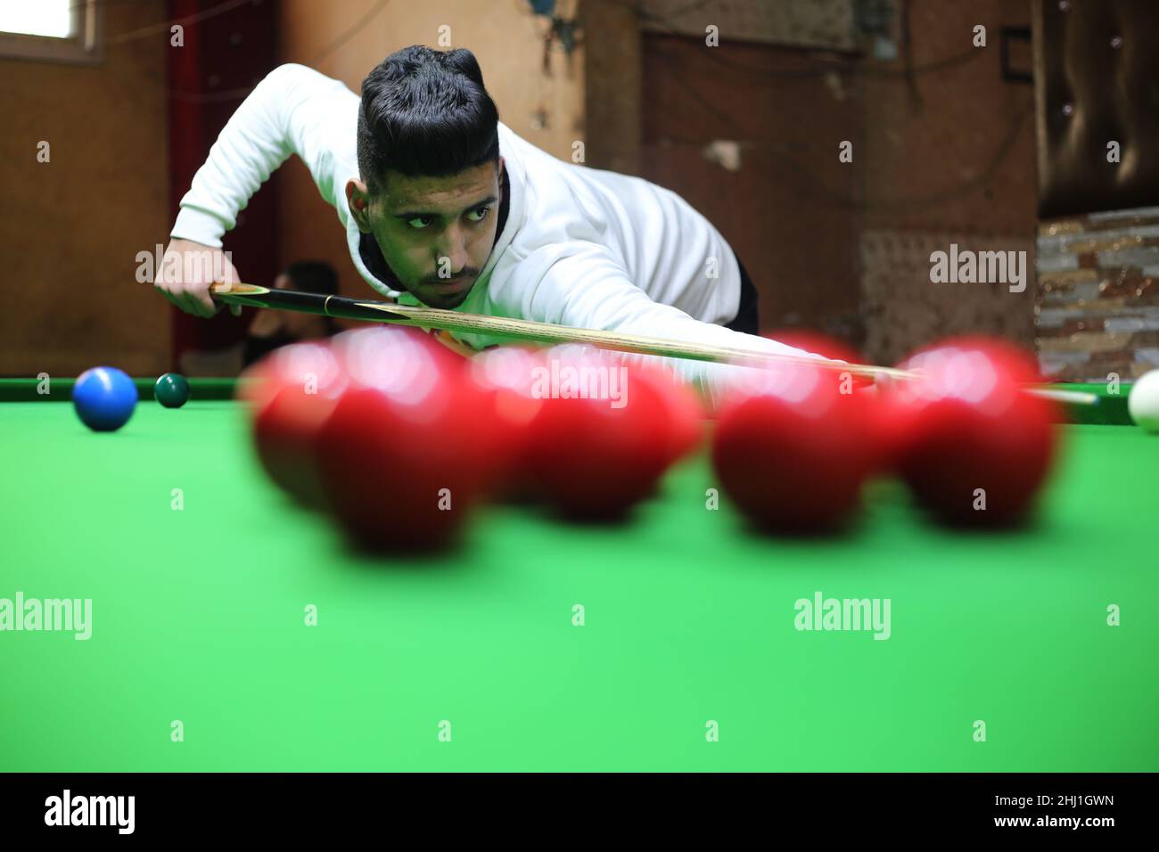 Gaza. 26th Jan 2022. Il giovane palestinese Ahmed Nasr gioca a snooker all'interno di un club sportivo locale nella città meridionale della striscia di Gaza di Rafah, il 26 gennaio 2022. Nasr, 22 anni, imparò a giocare a biliardo e snooker da suo padre, poi imparò le regole del gioco attraverso i video di YouTube. Recentemente ha vinto il primo posto nel campionato di snooker della striscia di Gaza, che lo ha qualificato per il campionato di classificazione a livello della squadra palestinese. Credit: Khaled Omar/Xinhua/Alamy Live News Foto Stock