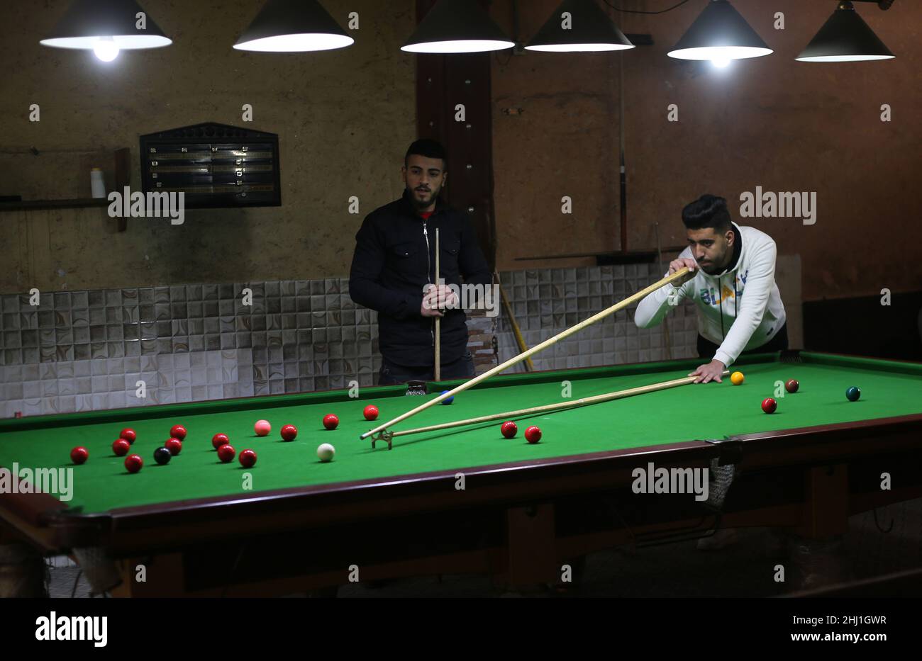 Gaza. 26th Jan 2022. Il giovane palestinese Ahmed Nasr (R) gioca a snooker all'interno di un club sportivo locale nella città meridionale della striscia di Gaza di Rafah, il 26 gennaio 2022. Nasr, 22 anni, imparò a giocare a biliardo e snooker da suo padre, poi imparò le regole del gioco attraverso i video di YouTube. Recentemente ha vinto il primo posto nel campionato di snooker della striscia di Gaza, che lo ha qualificato per il campionato di classificazione a livello della squadra palestinese. Credit: Khaled Omar/Xinhua/Alamy Live News Foto Stock