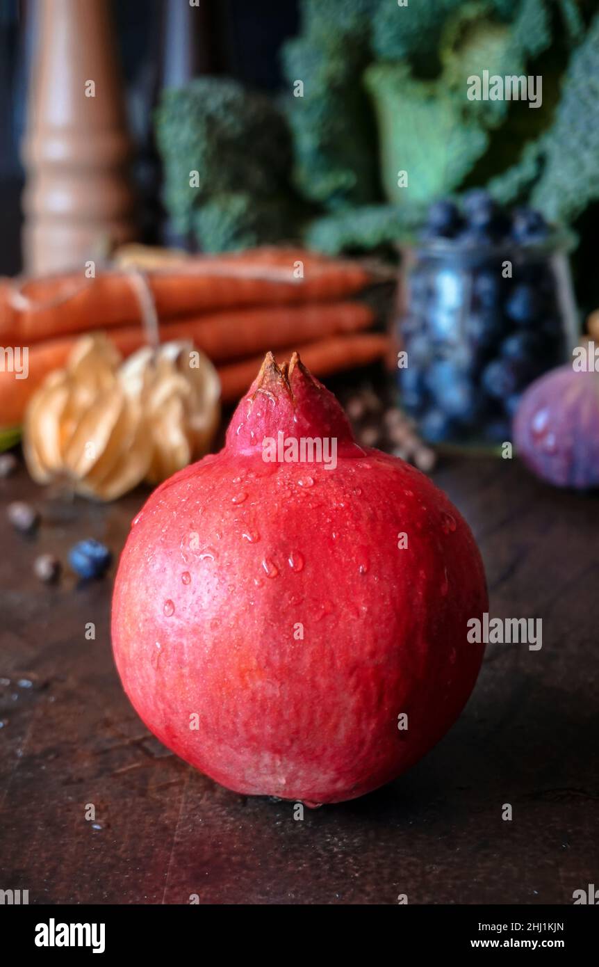 Una melagrana matura intera con gocce d'acqua sullo sfondo di verdure e bacche autunnali Foto Stock