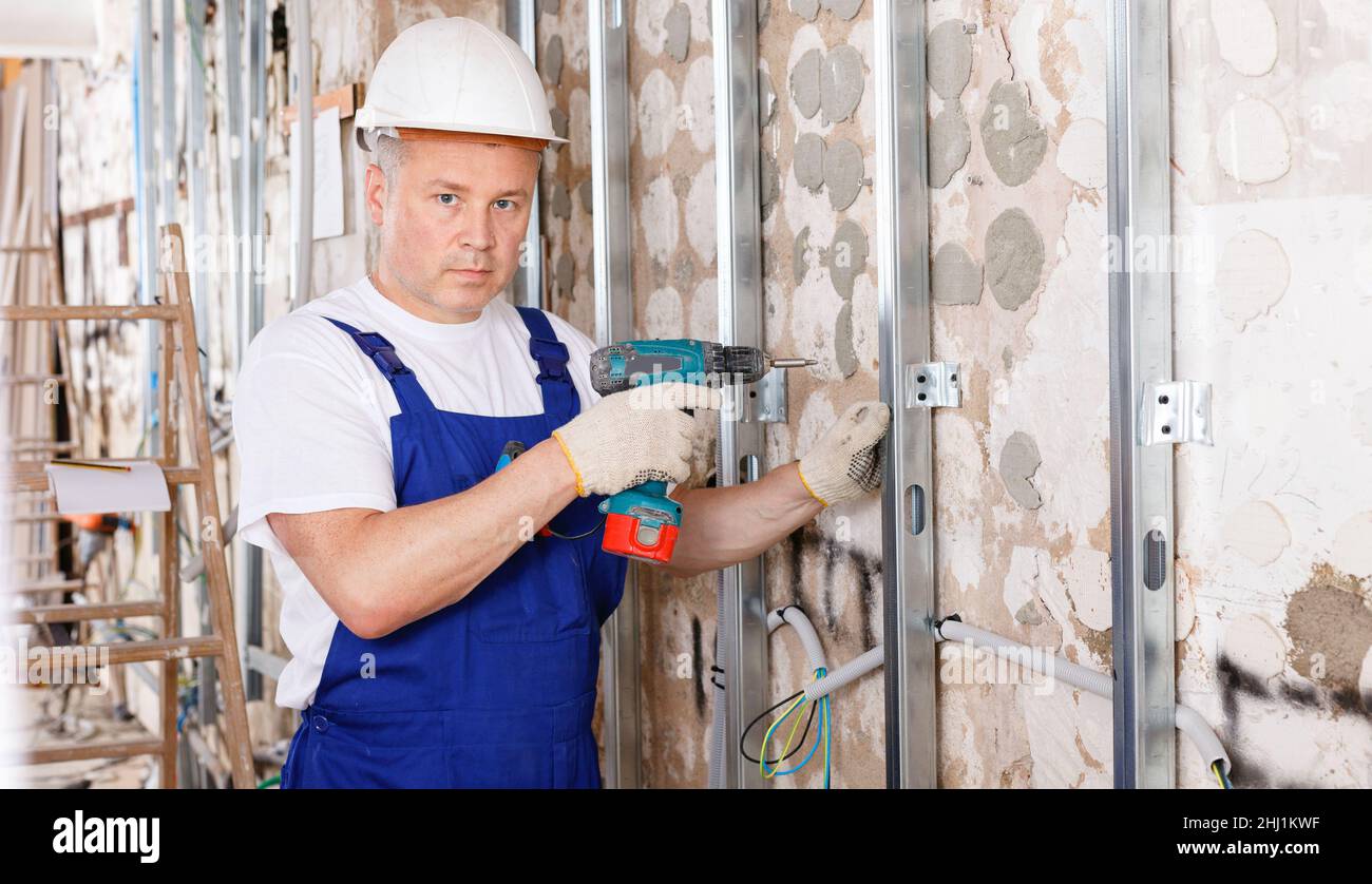 Operatore edile che utilizza una pistola a vite per il montaggio di profili in alluminio in cantieri interni Foto Stock