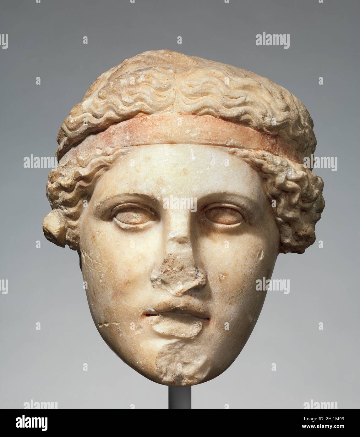 Testa di marmo di una divinità con filetto Dionisiaco ca. A.D.14–68 Copia romana di un'opera greca del 2nd secolo a.C. anche se la schiena e il collo sono tagliati via, la superficie rimanente di questa testa è in condizioni eccezionali, mantenendo il pigmento rosso sugli occhi, labbra e filetto, e tracce di doratura nei capelli. Altre copie romane di questa opera sono conosciute, così come una testa di marmo estremamente fine trovata nel 1886 sul versante sud dell'Acropoli ateniana, e ora nel Museo Nazionale, che la maggior parte degli studiosi hanno considerato l'originale greco. Qui, la testa viene ruotata e inclinata verso l'alto Foto Stock