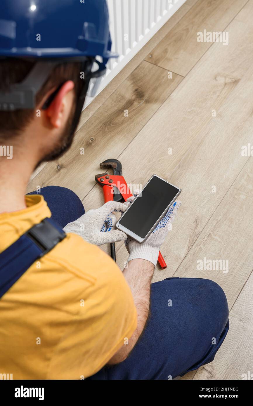un operatore in un casco arancione installa i radiatori in casa Foto Stock