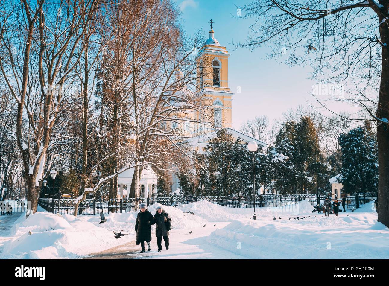Gomel, Bielorussia. Due donne che camminano nel Winter City Park. Famoso punto di riferimento locale è la Cattedrale di Pietro e Paolo sullo sfondo Foto Stock