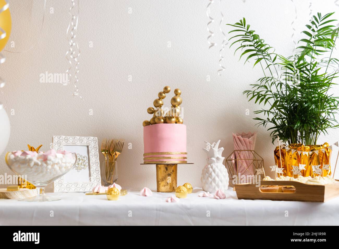 Tavolo di compleanno con torta e balloni. Decorazioni rosa e dorate Foto Stock