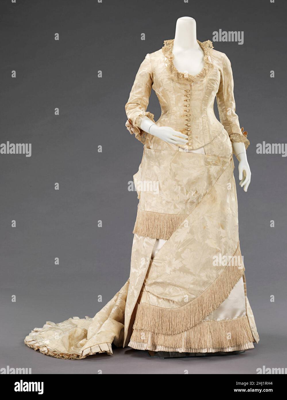 Abito da sera ca. 1880 Casa del valore francese questo abito grazioso degno è composto da un tessuto efficace con il sottile acorno e foglia di quercia motivo che significa stabilità, longevità e buona fortuna. La silhouette del trambusto, anche se associata principalmente alla seconda metà del 19th secolo, ha avuto origine in prima moda come un semplice urto sul retro del vestito, come con le mantuas fine 17th-inizio 18th secolo e fine 18th-inizio 19th secolo abiti Impero. La silhouette piena di trambusto ebbe il suo primo aspetto vittoriano alla fine del 1860s, che iniziò come pienezza in gonne movine Foto Stock