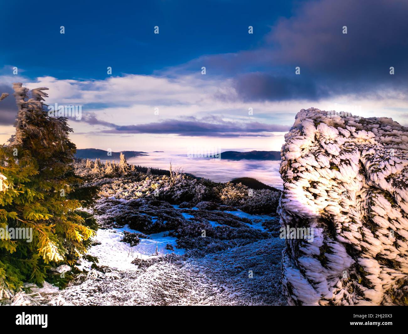 Paesaggio panoramico con alberi di abete rosso e roccia ricoperta di rime, vista da una gamma di mountatin alla valle piena di nubi basse e nebbia durante il temperat Foto Stock